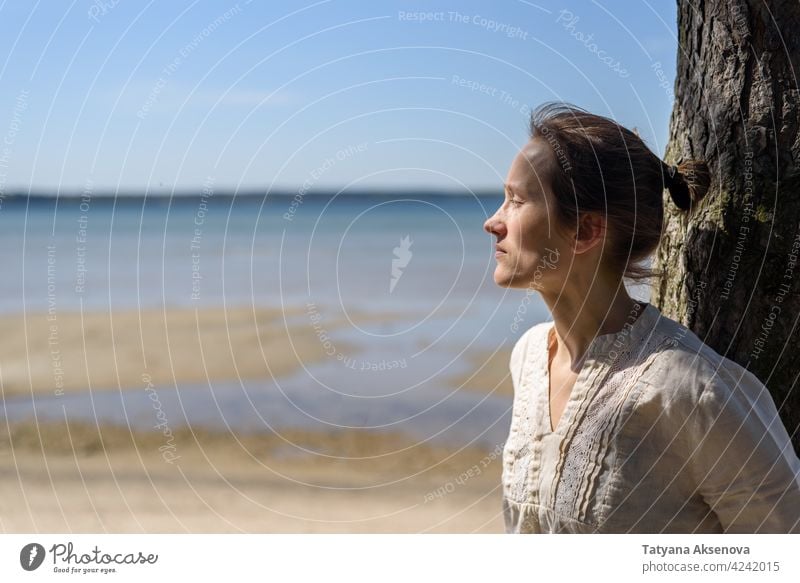 Woman sitting between trees and looking to sea woman nature outdoor wellbeing relaxation mindfulness breathing tranquility meditation person freedom lifestyle