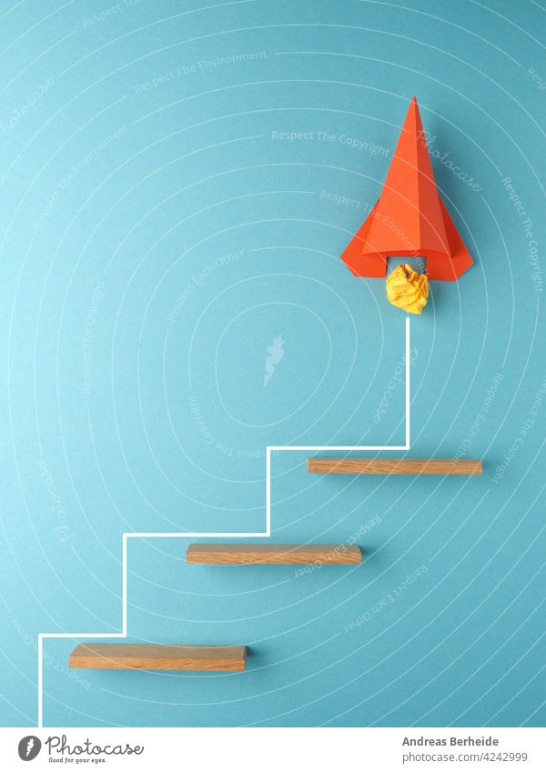 Orange rocket or starship climbing the stairs, upswing or startup concept Rocket crumpled paper ball action goal success financial business blocks message