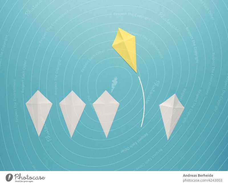 White paper kites in a row with a yellow paper kite flying away leader leadership action goal success financial business message marketing blue management