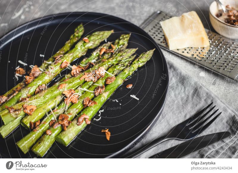 Baked asparagus with almond nut petals and cheese on black plate. baking roasted vegetarian food serving sause cutlery linen napkin gray table angle view