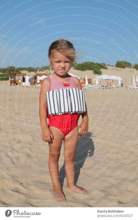 little girl stands on beach in a special swimsuit for children who can not swim. child in swimsuit, which he kept afloat portrait outdoor sun 3 recreation