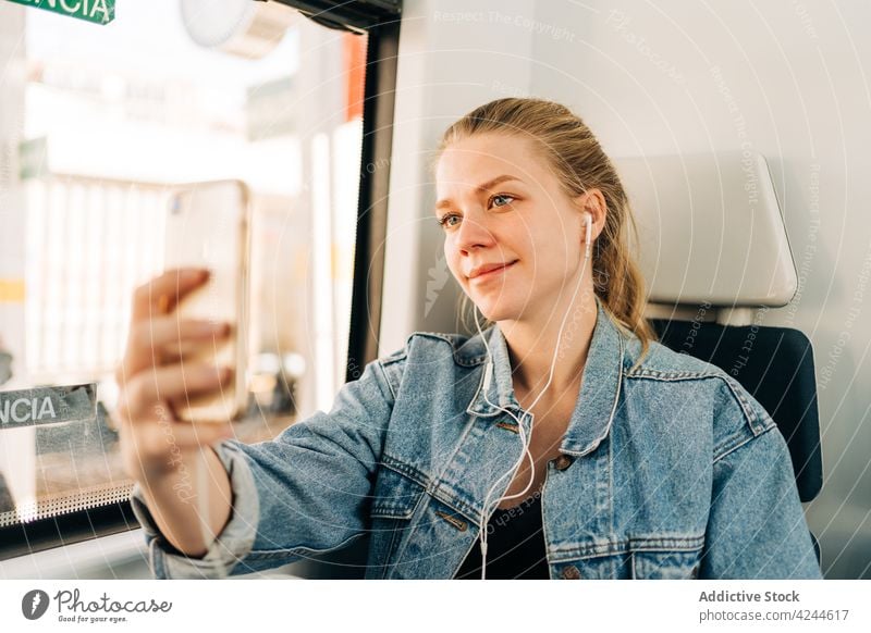 Smiling woman taking selfie in train ride commute music listen earphones smartphone passenger transport social media using mobile window young lifestyle modern