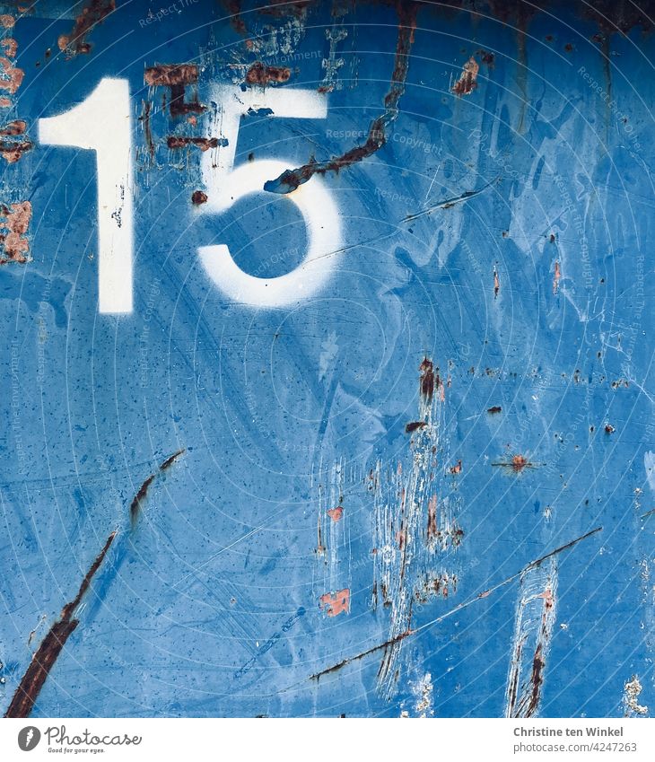 A white 15 on the scratched metal wall of a much used old blue container number fifteen digit Digits and numbers Metal metal facade Container traces of use