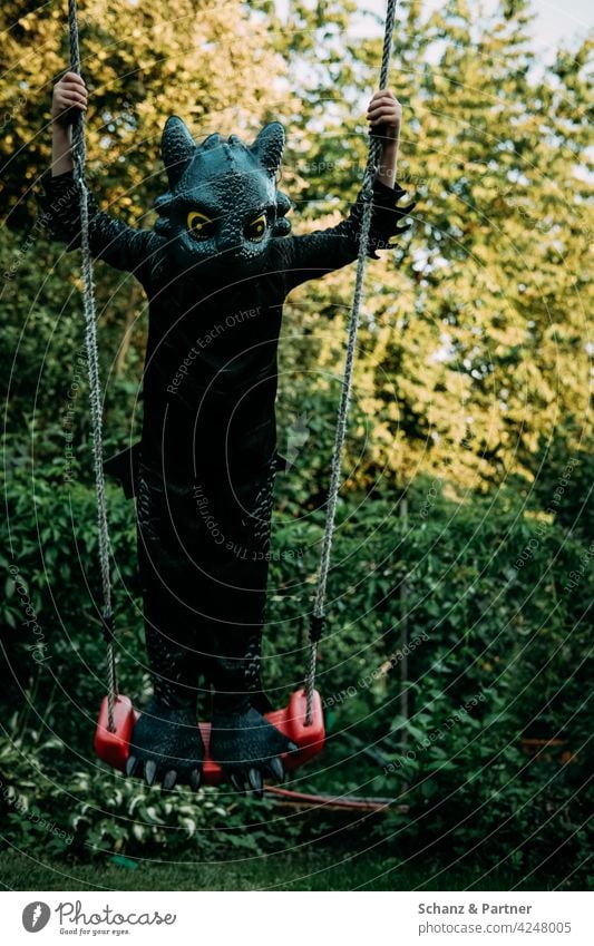 Child standing on the swing dressed as a dragon cladding Dress up carnival Costume Swing Dragon Toothless Black To swing Infancy Family family life Playground
