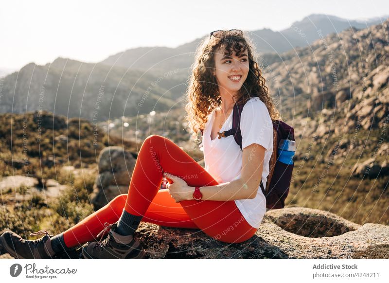 Smiling young woman sitting on stone and admiring nature in mountainous valley admire relax enjoy traveler vacation hike recreation positive journey female