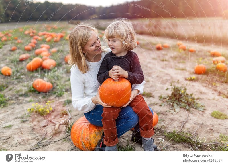 Mother and son in pumpkin patch field halloween nature park autumn fall woman female mother family parents boy kids children relationship together togetherness