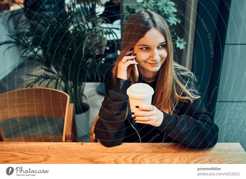 Young woman talking on the phone at cafe, having a pleasant phone call, answering call, chatting by mobile phone with friend while sitting in a cafe and drinking coffee. Girl relaxing in cafe