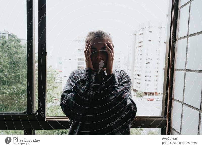 Worried woman looking from the window of her flat, mental health concept in the city, depression with copy space anxiety frustration problem sad sadness