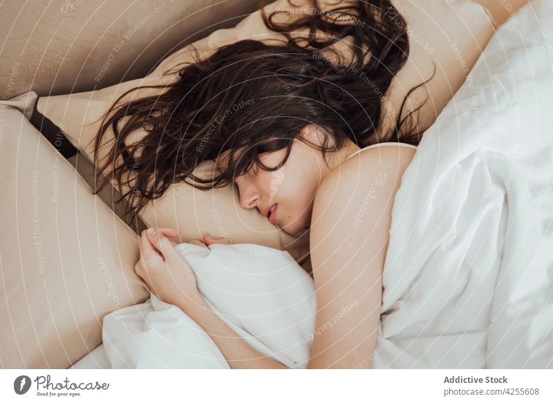 Young woman sleeping peacefully on cozy bed in morning comfort relax dream bed time asleep bedroom lying duvet lazy pillow nap eyes closed blanket at home