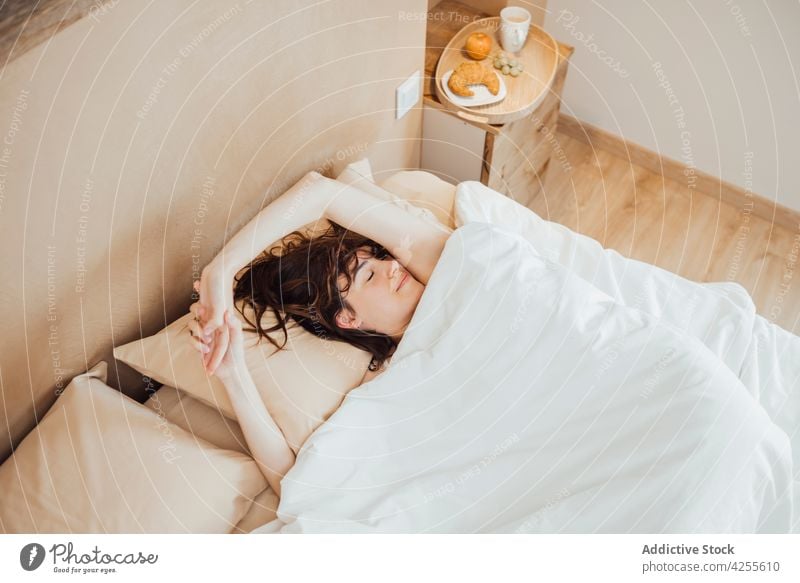 Young woman sleeping peacefully on cozy bed in morning comfort relax dream bed time asleep bedroom lying duvet lazy pillow nap eyes closed blanket at home