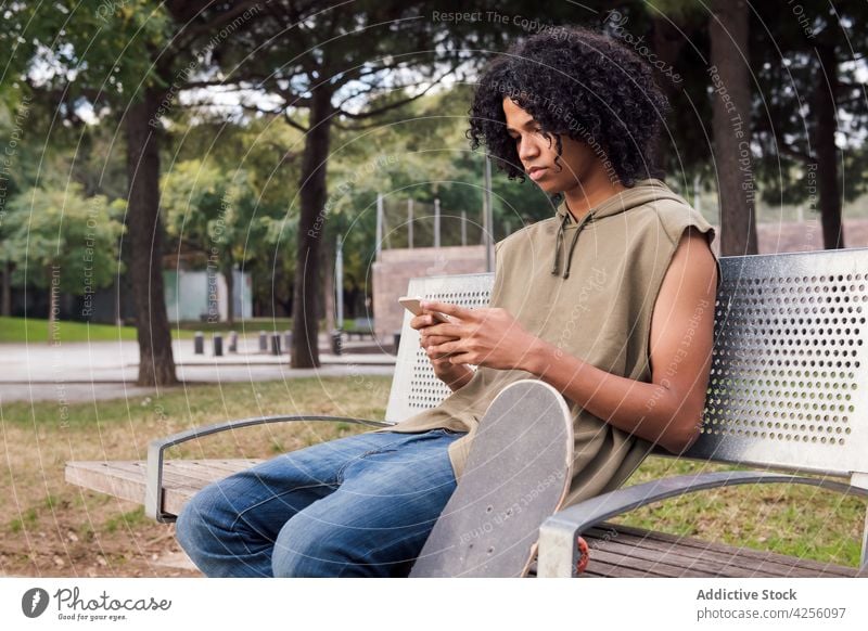 Black man sitting on bench and using smartphone internet skateboard break message park texting connection male browsing surfing online cellphone gadget read