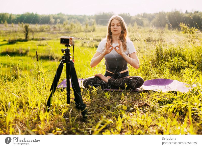 The girl practices yoga in nature and records a video lesson about yoga. Yoga online, training online camera pose healthy fitness lotus blogger blogging relax