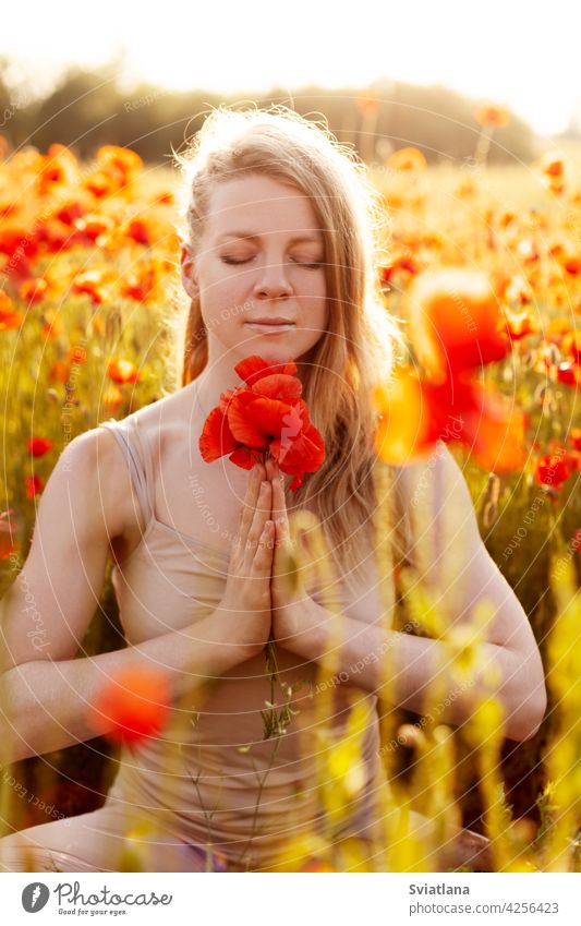 Portrait of a beautiful girl with a bouquet of poppies in her hands meditating on a poppy field. Yoga, Meditation, Mental health yoga woman meditate meadow