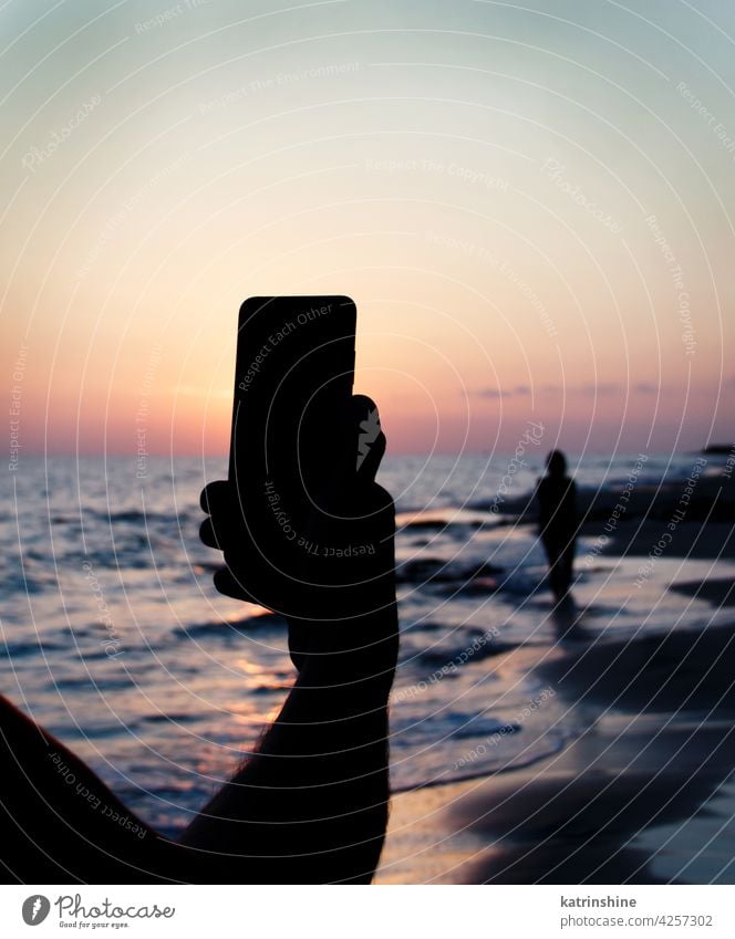 Man takes a sunset photo of girlfriend on the mobile phone sky sea men taking picture women silhouette faceless hand cellphone cellular nature outdoor cityscape