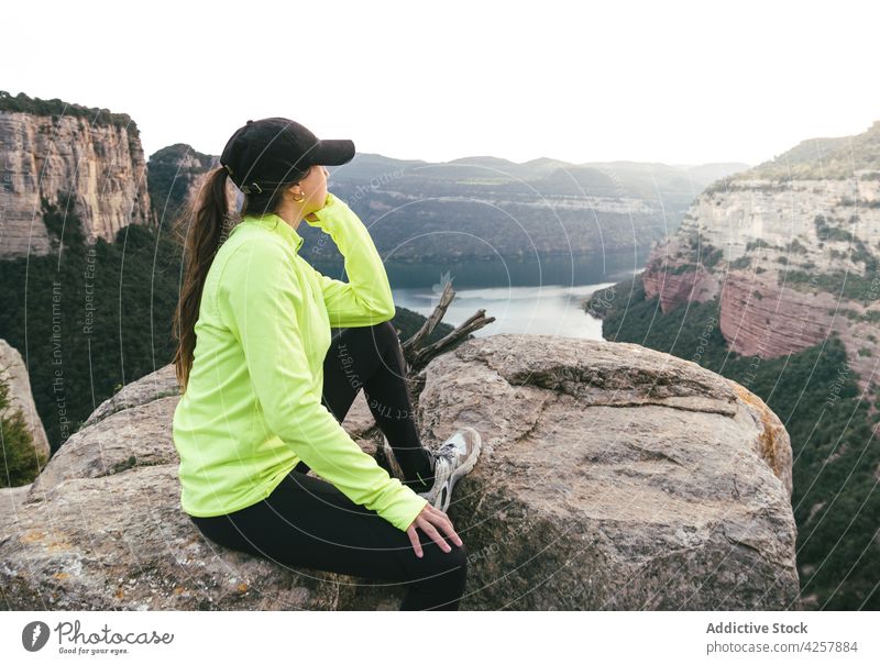 Young female traveler resting on rocky cliff and admiring nature woman admire mountain enjoy recreation hike explore holiday peaceful young long hair dark hair