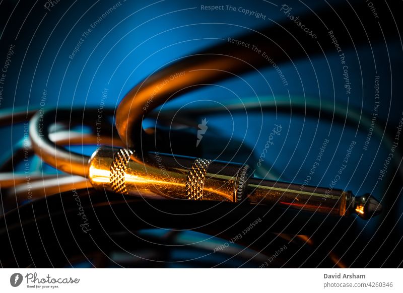 Macro Closeup of Metal Quarter Inch Instrument Cable Connector Laying Horizontally on Cord in Front of Teal Background with Orange Lighting quarter inch jack