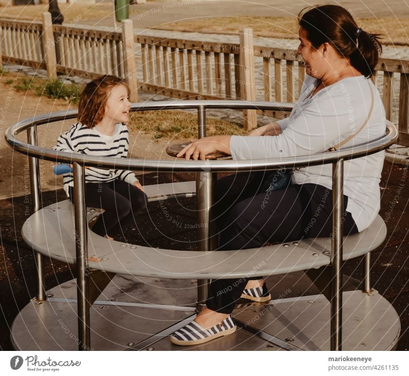 Mother and daughter having fun with a spinning wheel at a children's playground mother complicity females two people playing colours outdoors girls move
