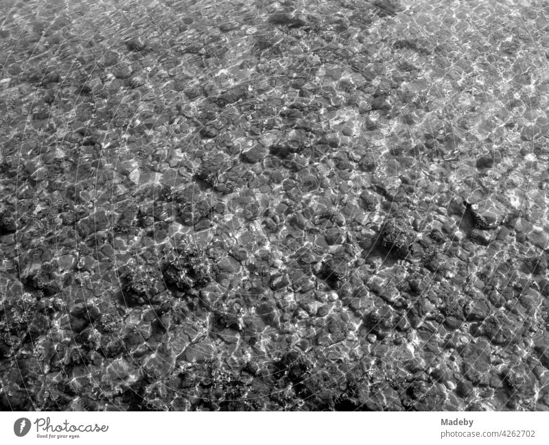 Shallow water with stones at the beach in Alacati near Cesme in the province of Izmir at the Aegean Sea in Turkey, photographed in classic black and white Water