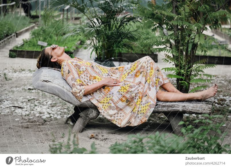 Woman in dress lying relaxed on a wooden lounger in a garden pretty Lie Couch Garden Dress vacation chill Summer voyage Vegetable bed plants Green Nature