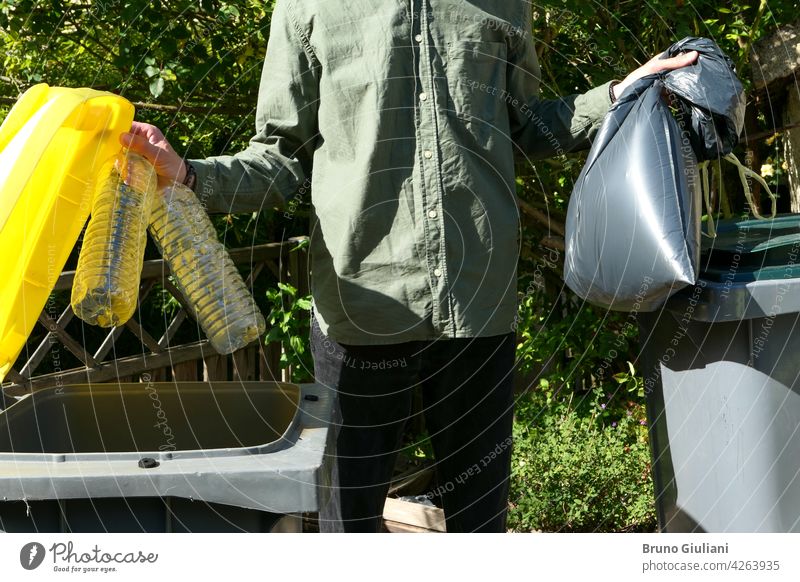 One person performing a selective sorting of household waste in recycling bins. Man putting plastic bottles in a yellow container and garbage in a bag in a green container.