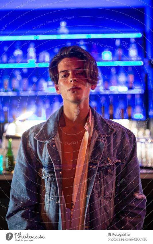 Portrait of young man in jean jacket with bar background. model look white casual attire standing light side smile boy hold face behind person people attractive
