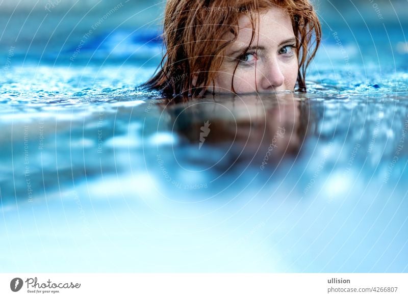 Portrait of young sexy woman with red hair, redhead swimming in the pool, head half submerged under water, copy space wet summertime enjoyment attractive