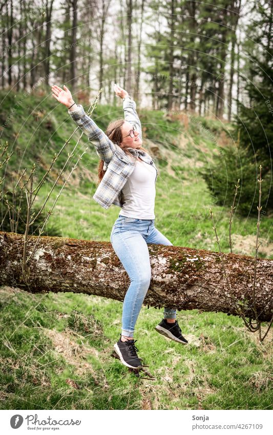 Young woman with raised arms sitting on a tree trunk in the forest Tree trunk Sit Joy Laughter Happy Happiness Exterior shot Forest Joie de vivre (Vitality)