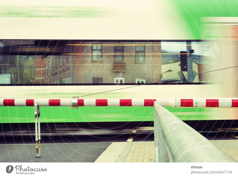 A train passes a closed level crossing, houses are reflected in its windows / motion blur / travelling / rail traffic Train Railroad crossing Train travel Track