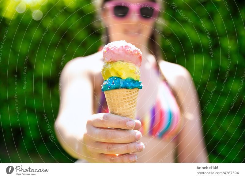 young female in rainbow colored swimwear giving ice cream, two colorful different flavors ice cream scone in hand with sprinkles in the summer, food,spring,Holiday,vacation concept