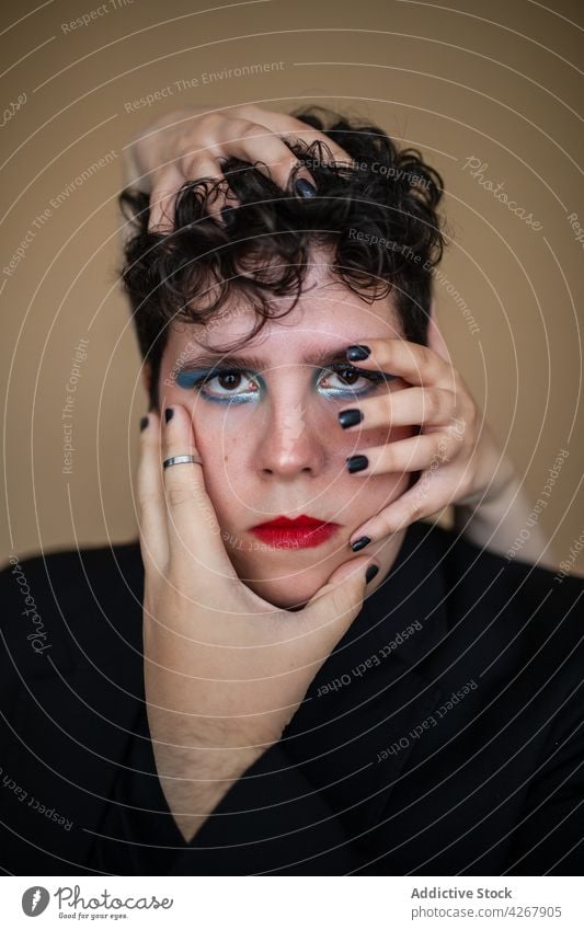 Androgynous male under hands of woman touching face makeup eccentric style feminine queer unusual transgender alternative provocative equal extraordinary accept