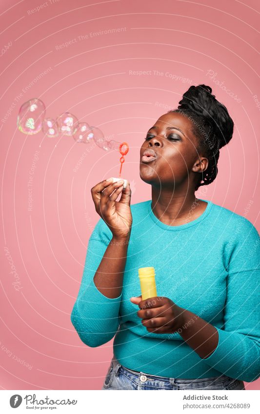 Joyful black woman blowing soap bubbles in studio ethnic joyful african american happy colorful vivid playful toy having fun smile entertain positive cheerful