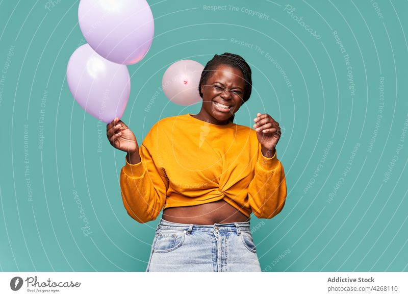 Joyful black woman playing with balloons in studio excited happy joyful playful laugh eyes closed vivid having fun style colorful cheerful bright stand outfit