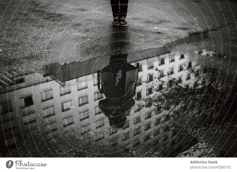 Person in outerwear standing on street and reflecting in puddle person reflection wet facade asphalt building gloomy rain overcast road path urban district