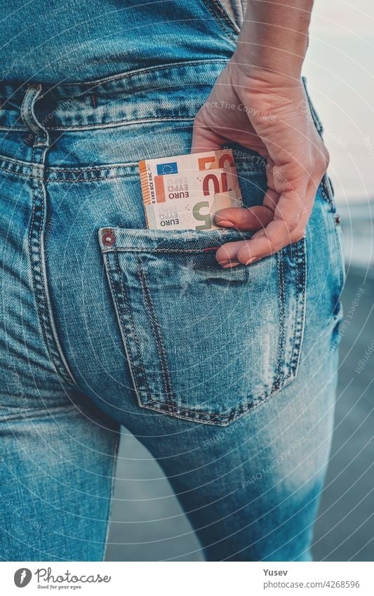 A woman's hand takes out euro bills from the back pocket of her jeans. The concept of finance, savings, financial expenses. Close-up taking banknote blue money