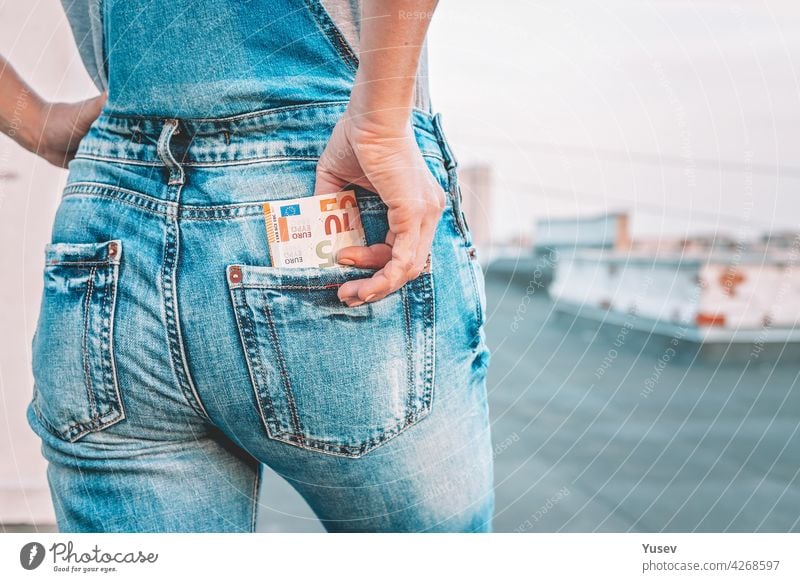 A womans hand takes out euro bills from the back pocket of her jeans. The concept of finance, savings, financial expenses. Close-up. Copy space taking banknote