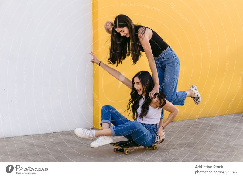 Happy sisters having fun while riding skateboard on pavement ride sport leisure recreation cheerful legs crossed together sibling smile carefree sneakers denim