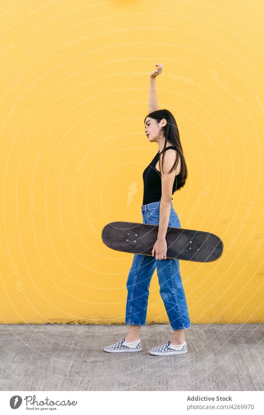 Skateboarder in casual apparel on pavement on yellow background skater skateboard arm raised cool contemporary generation spare time lifestyle teen equipment