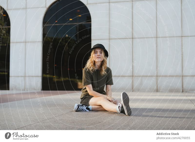 Cool woman in hat resting on city pavement cool individuality street style legs crossed contemporary generation walkway town portrait lifestyle architecture