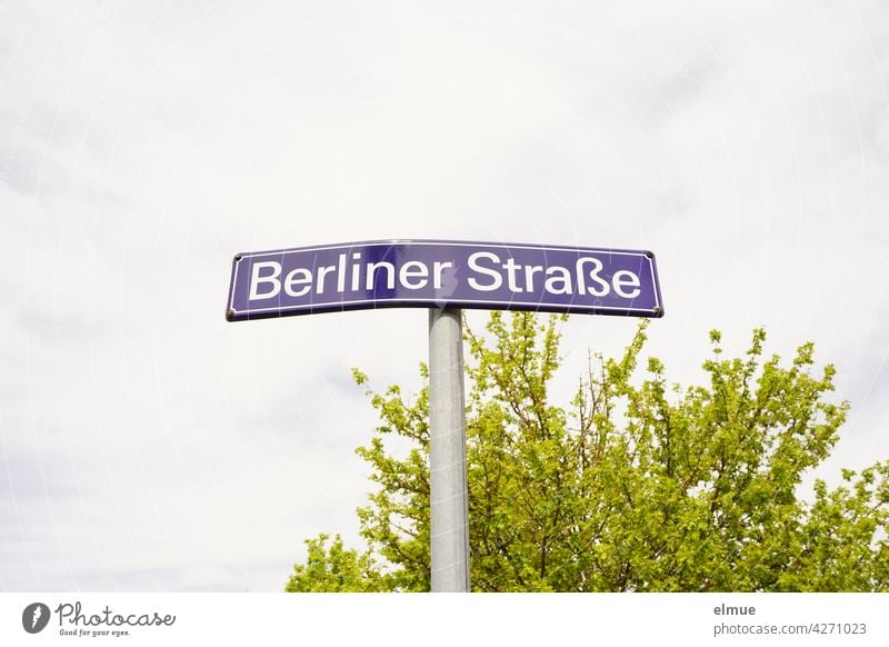 bent street name sign " Berliner Straße " in front of a green bush and cloudy sky Street sign street sign Orientation berlin street Bend corrupted dwell Central