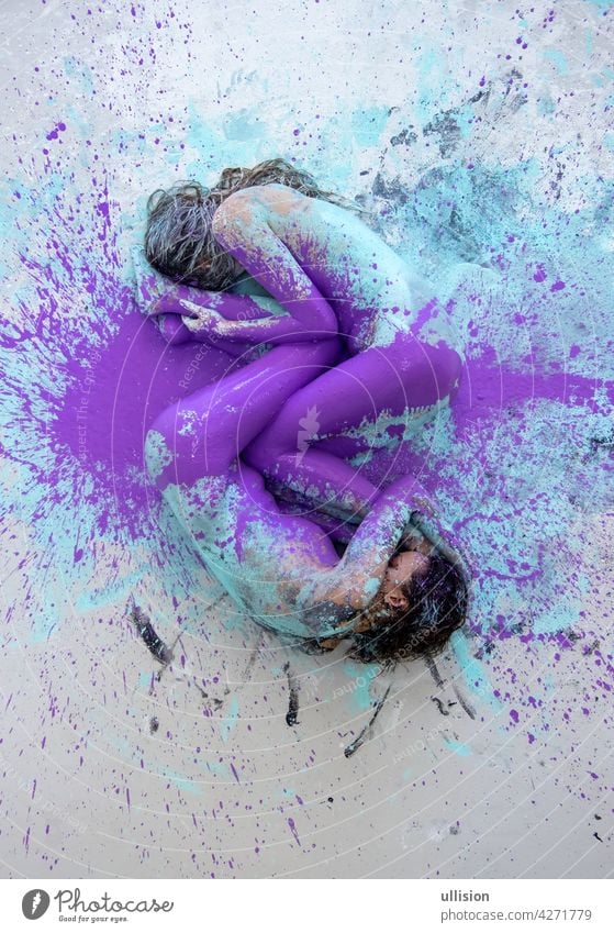 Two artistically abstract painted young sexy women, girlfriends in pink, purple, turquoise and white color lying like a Yin Yang symbol on the floor in the studio, copy space.