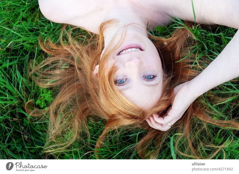 smiling portrait of a beautiful young sexy redhead woman spreading red hair fan-shaped lying relaxing on the green grass, upside down, copy space Portrait