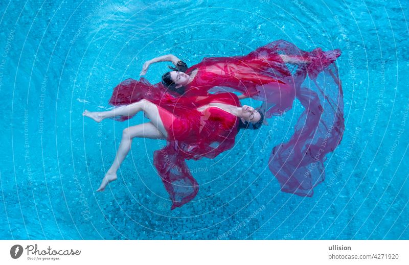 Top view of a beautiful young sexy dark-haired women relaxed in red dress floating weightlessly elegant in the water of the pool, copy space two swimmer girl