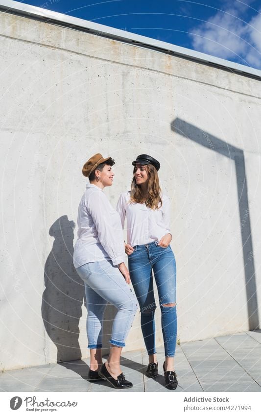 Smiling women standing on pavement near stone fence smile street friend stone wall trendy girlfriend laugh female young shadow bright sunny best friend town