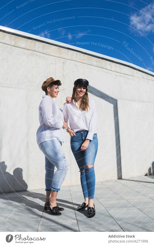 Smiling women standing on pavement near stone fence smile street friend stone wall trendy girlfriend laugh female young shadow bright sunny best friend town