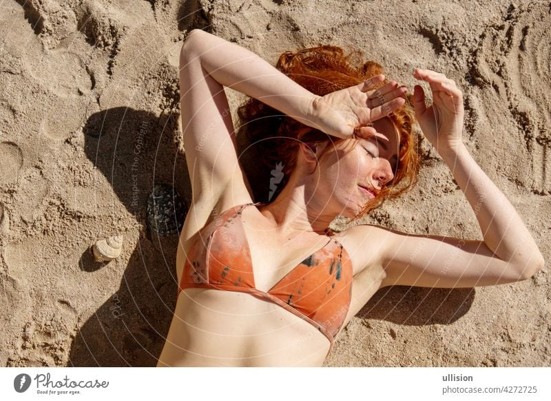 Overhead shot of a sexy redhair bikini woman redhead laying in the sunshine on the sand on the beach portrait skin outside pale seductive summertime outdoors
