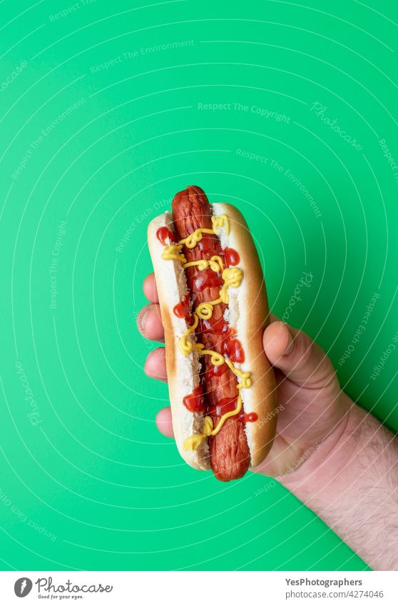 Hot dog held in man hand on a green table, top view. above american arm background bread bun calories color copy space cuisine cut out delicious eat fast