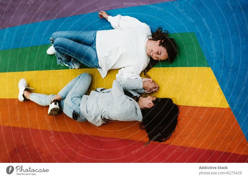 Happy female couple lying on colorful floor and holding hands women fun lgbtq laugh joy pride lesbian carefree having fun together positive relax happy cheerful