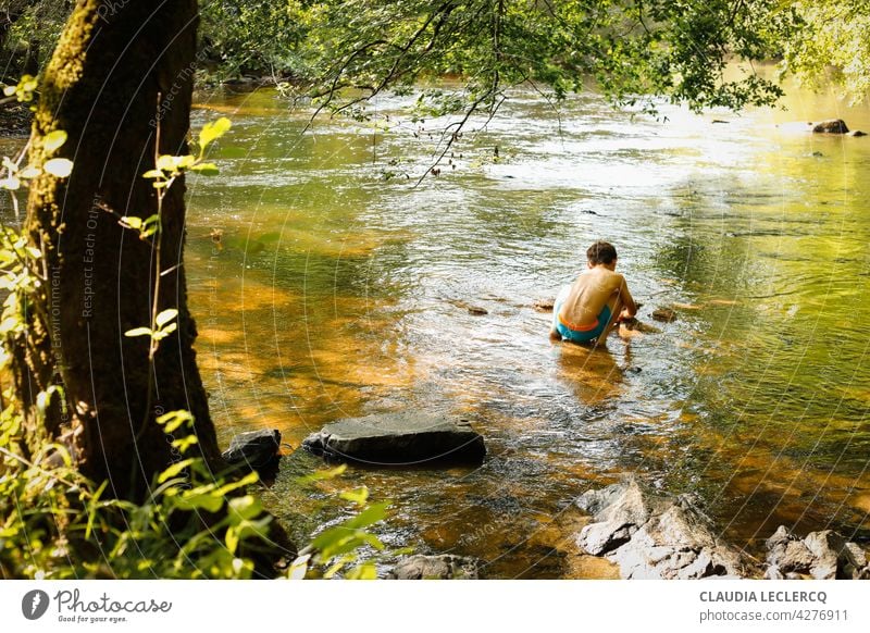 Young boy sitting and playing in the river back view young boy sitting River lifestyle male person kid people cute portrait education Playing learning nature