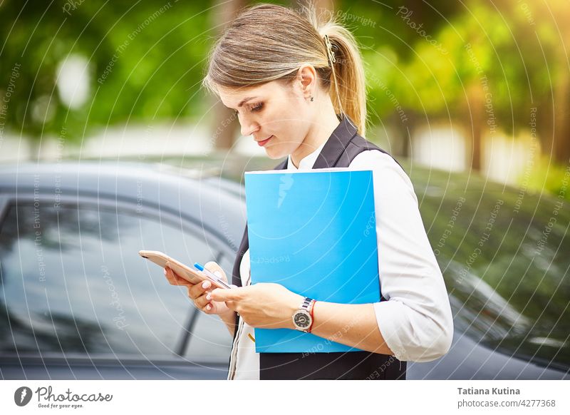 A young business woman with a folder for papers in her hands looks at her smartphone businesswoman texting manager person busy professional office female