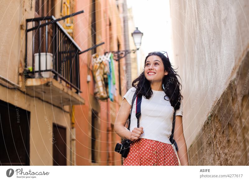 Young happy tourist woman walking down an european city alley with a camera travel vacation girl holiday lane backstreet backpack old town summer spring one